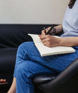 A woman on a sofa speaking to a therapist who is taking notes on a legal pad