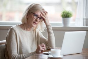Thoughtful confused mature woman looking at laptop, suffering from memory loss